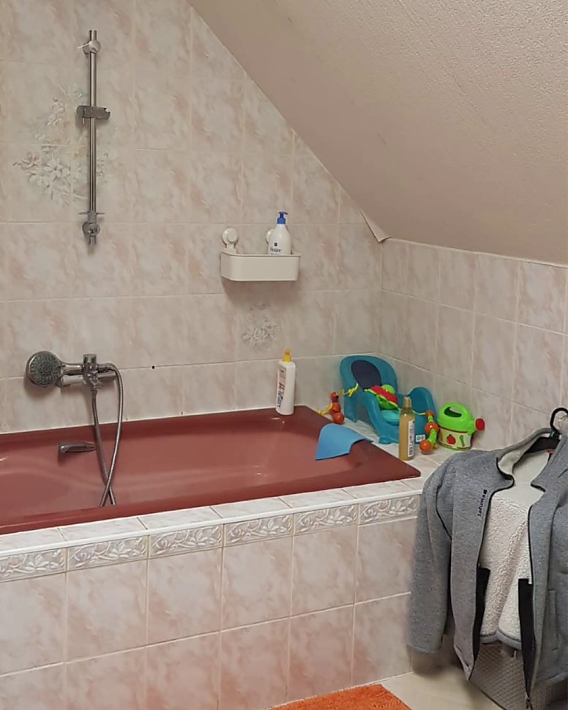 Salle de bain sous combles avant redécoration, avec un carrelage rose et une baignoire rouge